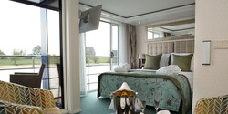 A Category Suite room, featuring a double bed, club chairs and a sliding balcony door leading to an outdoor seating area. A Category Suite room, featuring a double bed, club chairs and a sliding balcony door leading to an outdoor seating area.