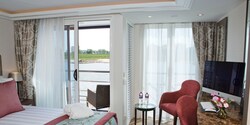 A Category AA room, featuring a double bed, two club chairs and a sliding balcony door leading to an outdoor seating area. A Category AA room, featuring a double bed, two club chairs and a sliding balcony door leading to an outdoor seating area.