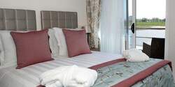 A Category BA room, featuring a double bed and a table with chairs, outside of a sliding balcony door. A Category BA room, featuring a double bed and a table with chairs, outside of a sliding balcony door.