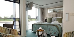 A Category Suite room, featuring a double bed, club chairs and a sliding balcony door leading to an outdoor seating area. A Category Suite room, featuring a double bed, club chairs and a sliding balcony door leading to an outdoor seating area.
