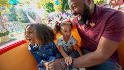 A dad and his 2 young daughters laugh while riding the Mad Tea Party attraction