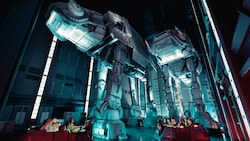 People in a transport vehicle inside a hanger bay look up at 2 towering AT-AT walkers