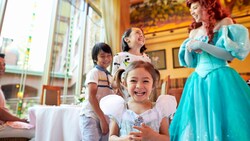 Una niña pequeña sonríe mientras su hermano y hermana se ríen con la Princess Ariel de fondo