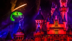 Sparkles fly in the night by a large projected image of Maleficent, next to Sleeping Beauty Castle during Halloween Time at the Disneyland Resort