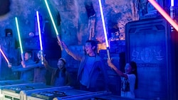 Five Guests standing around a circular table holding up their custom, hand-built lightsabers at Savi's Workshop