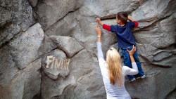 A mother helps her kid climb a rock to reach the Finish sign on the Redwood Creek Challenge Trail