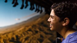 A teenager enjoying Soarin' Over California, with the legs of other Guests dangling above him