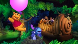 Pooh Bear floats with a balloon above Eeyore and Gopher while Guests travel in a giant honey pot