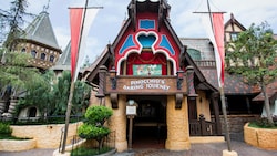 The outside of Pinocchioâ?s Daring Journey attraction at Disneyland park is styled like a storybook house with 2 stone columns on either side of an entranceway and an ornately carved balcony above it that resembles a marionette stage where a figure of Pinocchio is posed