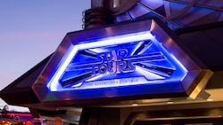 As night falls, the illuminated entrance sign for Star Tours The Adventures Continue welcomes Guests