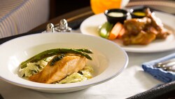 A succulent slice of salmon and 2 asparagus spears sit atop a bed of rice next to another dinner dish