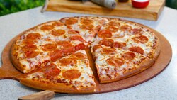 Una porción de pizza de pepperoni recién sacada del horno en una tabla de madera sobre una mesa al aire libre