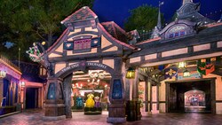 A shop with a half-timber style facade, a sign that reads 'Fairy Tale Treasure' and merchandise that includes ornate princess dresses for children, next to a tunnel with a sign that reads 'To Frontierland'