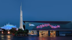 The exterior of Star Trader lights up in evening as spires atop Space Mountain extend toward the sky