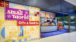 A simple shop with a sign that reads "small world Gifts & Sundries" selling Disney-themed swimwear, sunscreen, towels, batteries, novelty electric fans and souvenirs