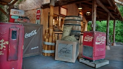 Old-looking crates, sacks, barrel and Coca-Cola® cooler near the entrance of Refreshment Outpost