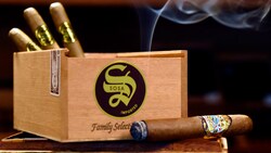 Un cigare allumé sur des cartons empilés de cigares Sosa