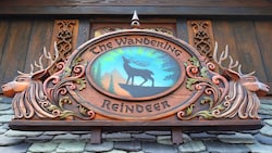 A wood carved sign on a shingle roof reveals a reindeer silhouette and the engraved words The Wandering Reindeer