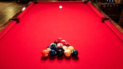 A red pool table with balls racked up and cue ball in position