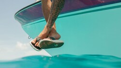 The legs of a person wearing flip flops dangling off the edge of a boat