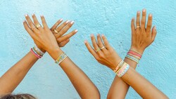 Two pairs of hands raised in the air, wearing an assortment of rings and bracelets from Pura Vida