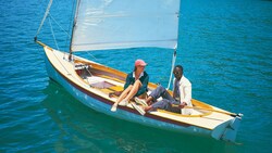 A woman and a man wearing boat shoes and casual attire relax in a sail boat on calm water