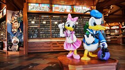 Statues of Donald Duck and Daisy Duck in front of a large display of Disney Pins and a sign that says ‘Welcome Pin Traders’