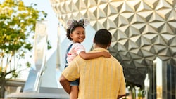 A father holding his smiling young daughter in his arms as he walks towards Spaceship Earth at Epcot