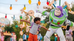 A young boy wearing space ranger gear standing next to Buzz Lightyear pretending to fly