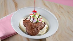 A Mickey Brownie Sundae, which features a brownie shaped like Mickey Mouse in a bowl of ice cream with a cherry, whipped cream and other toppings