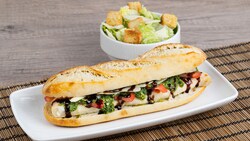 Chicken Caprese Baguette Sandwich with pesto and balsamic drizzle alongside a Caesar Salad