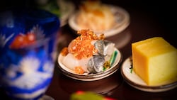 A plate of sliced fish and other food items on a table from Takumi Tei