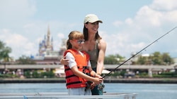 A girl wearing a life vest casts a fishing line with support from her mother