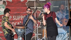 3 members of a 4 person band play guitar, bass and drums while the fourth members sings