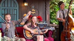 A trio of musicians performing with a guitar, fiddle and upright bass on a cozy stage in the Germany Pavilion at EPCOT