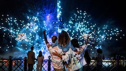 Two parents hold their young daughter as they watch a fireworks show over Epcot