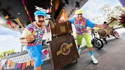 Variety performers Max & Aydar holding horns and standing next to a podium and touring tricycle at Epcot