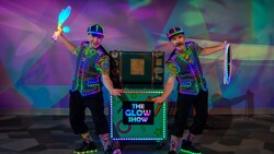 Max & Aydar, performers with glowing props next to a cart with a sign that reads, ‘The Glow Show’