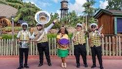 Five musicians from the jazz band Nola's Eight Note posing in front of the Tiana’s Bayou Adventure attraction at Frontierland