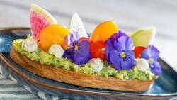A thick slice of avocado toast topped with grape tomatoes and garnished with fresh flowers