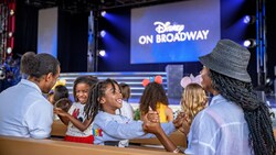 A seated family and a projector on stage with the words, ‘Disney on Broadway’