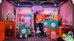 A puppeteer operating a marionette on a stage filled with holiday presents and decorations