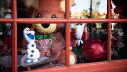 A teddy bear, a nutcracker and a figurine of Olaf in a store window