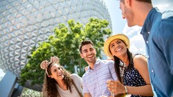 A group of 4 friends smiling as they enjoy festival food and drinks near Spaceship Earth in EPCOT
