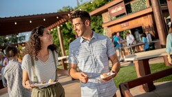 A man and woman holding small plates of food, smiling as they walk past a Global Marketplace kiosk