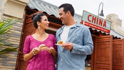 A couple with plates of food near a sign reading China, EPCOT International Food and Wine Festival