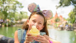 A smiling girl holding a cup of Dole Whip and wearing a Minnie Mouse ear headband