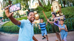 A dad takes a selfie while his kids hold lightsabers in front of a statue of Artoo Deetoo