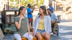 Two girls sit side by side, laughing in Star Wars: Galaxy's Edge in Disneyland Park.