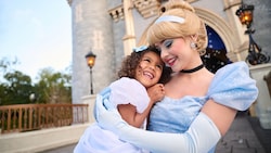 Cinderella holding a young girl in her arms in front of Cinderella Castle
